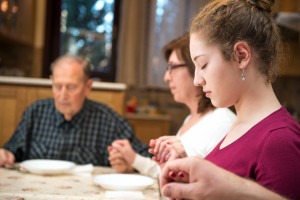 Family members join hands in prayer at Thanksgiving meal.