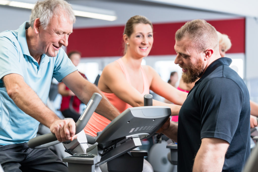 Senior man participating in spinning group at the gym with a personal trainer.