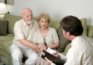 A senior couple talking with a marriage counselor. Could also be a salesman in their home.