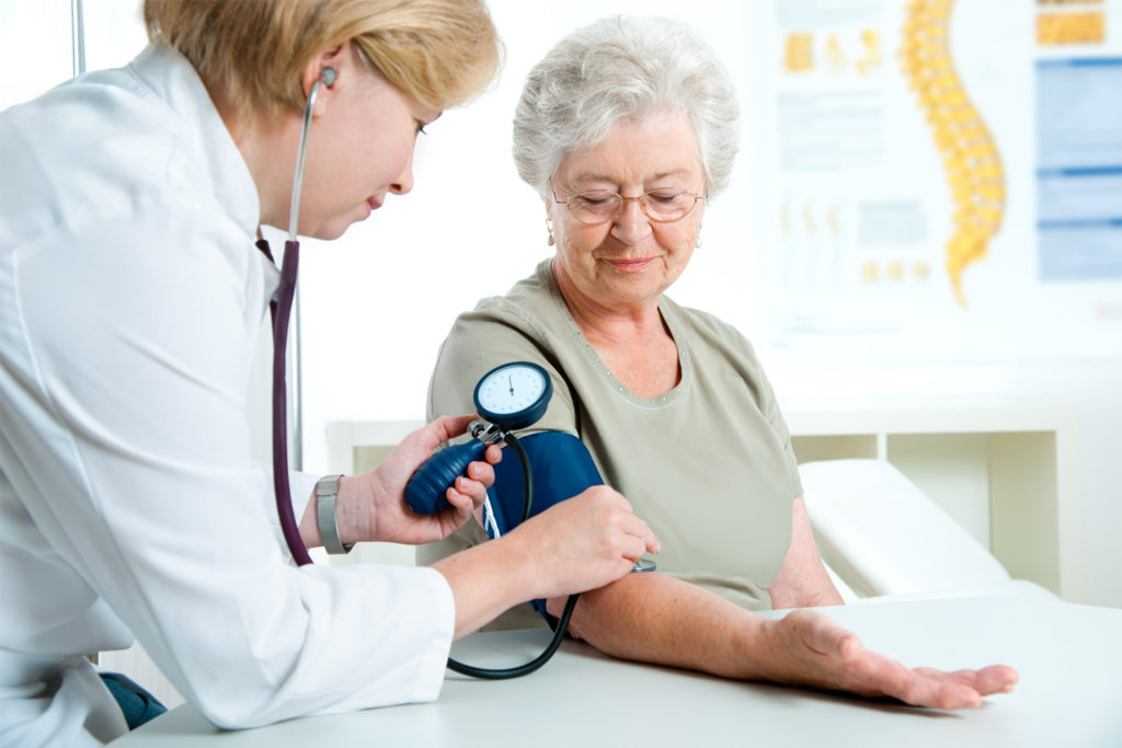 Nurse-clinician takes blood pressure reading of senior woman in medical office.