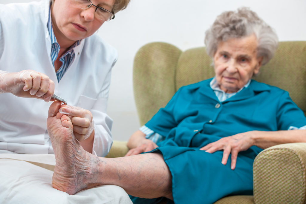 Nurse provides professional foot care services for elderly woman in home.