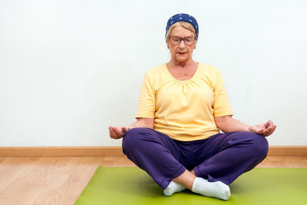 Elderly woman practicing yoga in gym.