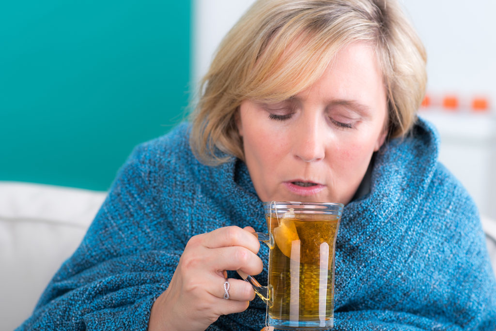 Senior sipping hot tea with lemon to help with her flu symptoms