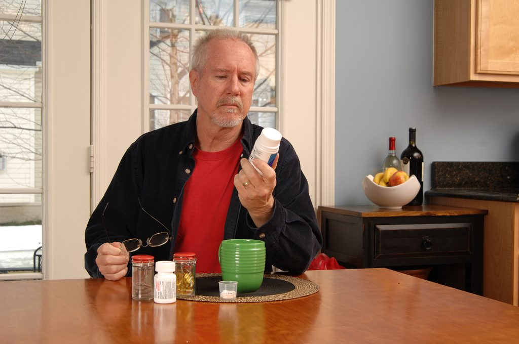 Senior man reading medicine bottle label at kitchen table.