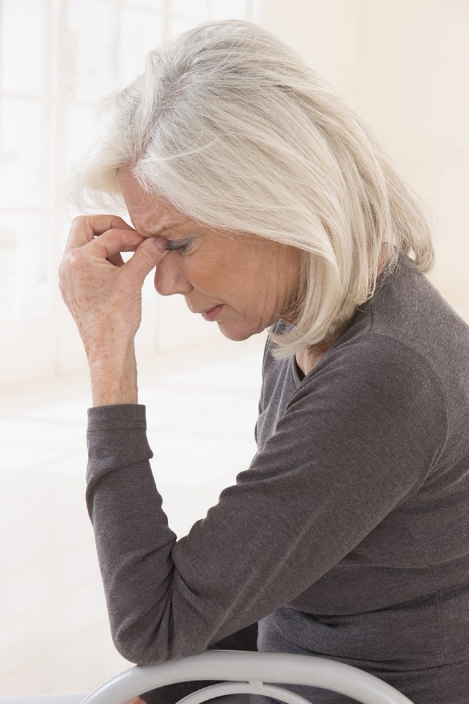 Senior woman in grey sweater holding her head with eyes closed in pain.