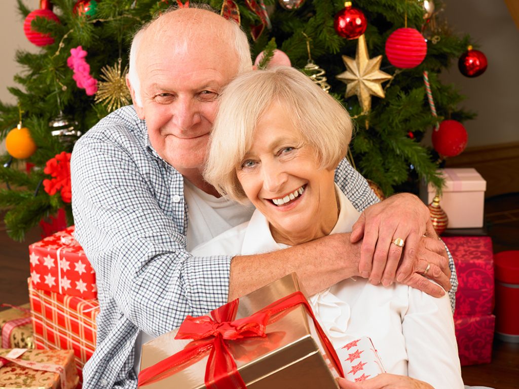 Senior couple hugging each other in front of the Christmas Tree.