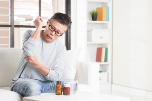 Mature Asian man holding his painful elbow. while getting ready to take his pain meds.