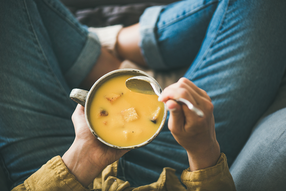 Woman with a warm mug of pumpkin cream soup with croutons, top view. 