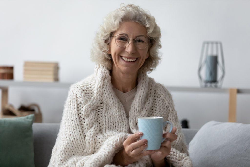 Head shot portrait smiling mature woman wearing glasses holding mug