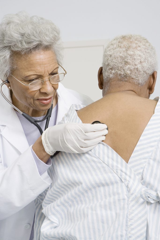 Senior female doctor checking patient's heart and lungs using stethoscope in clinic.