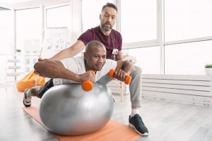 Physical therapist working with a young man on a balancing ball to help with pain management.