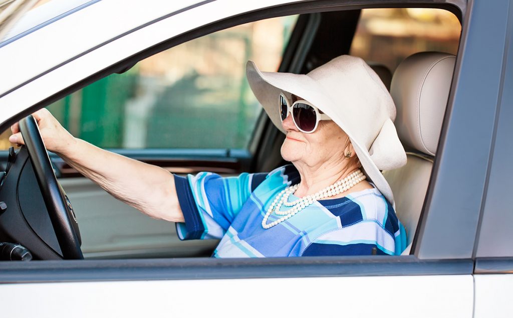 Senior woman in sunglasses and big hat out driving on a sunny day.