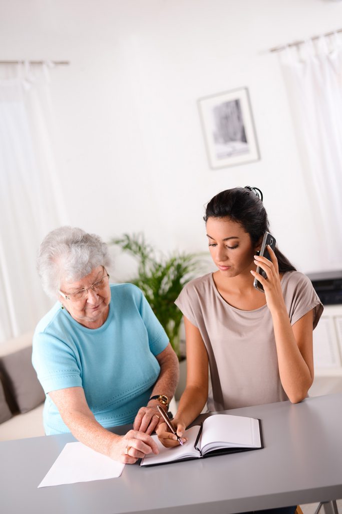 Young adult granddaughter helping her grandmother pay bills at a desk.