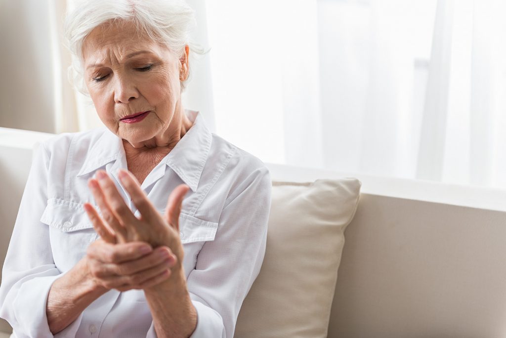 Senior women looking concerned and massaging aching hand joints.