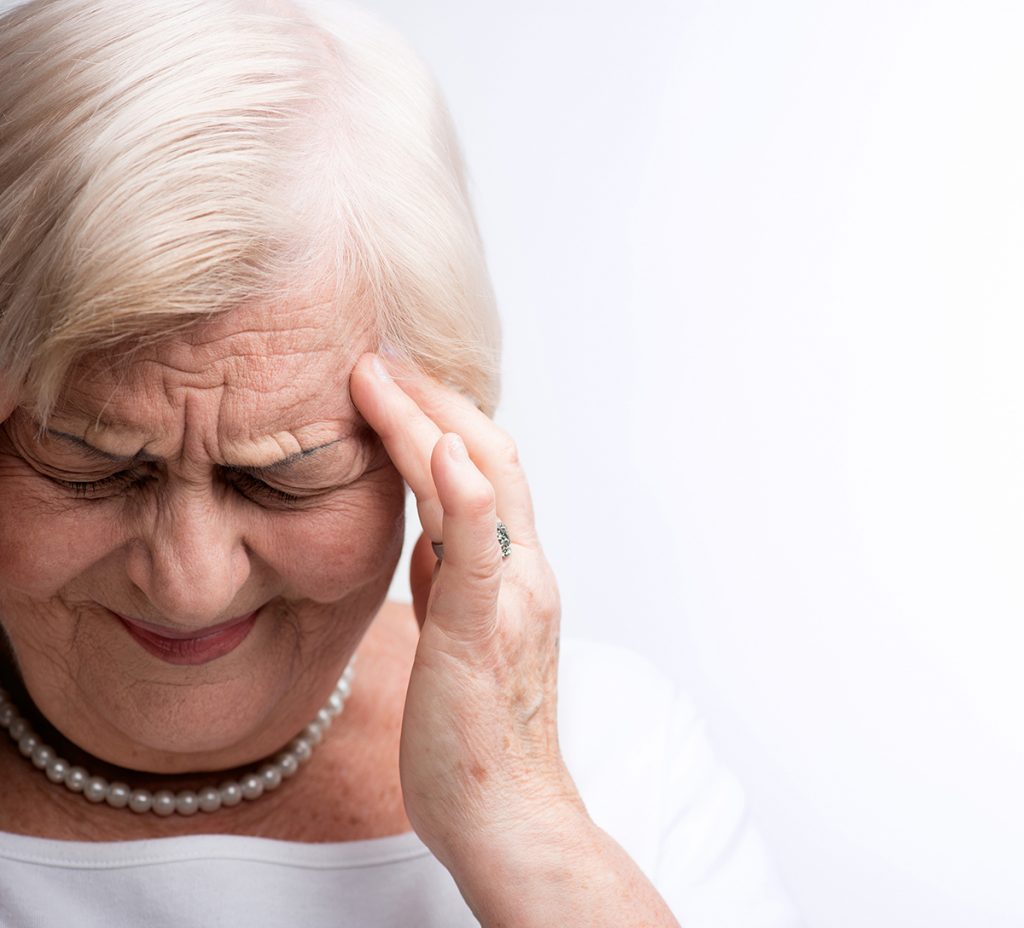 Elderly woman squinting and holding her forehead as if with a headache.