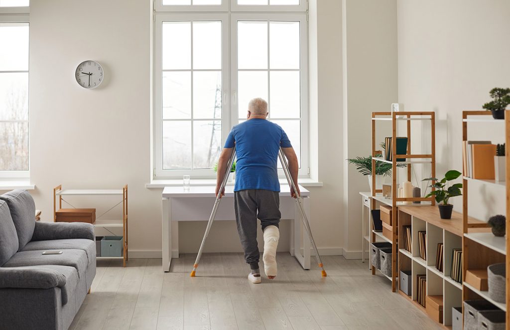 Senior man on crutches looking out winter window.