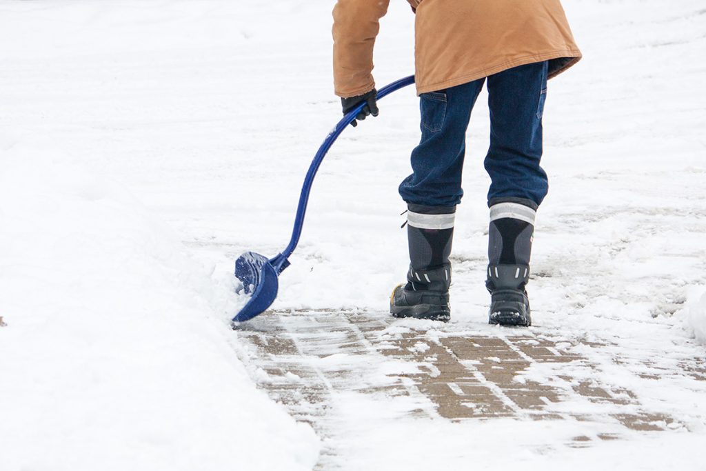 Man wearing warm coat, jeans and boots shovels walkway.