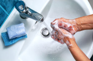 Thorough hand washing with sudsy soap and hot water over bathroom wash basin.