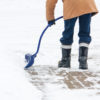 A man with a curved handled snow shovel clearing snow from a brick sidewalk in Canadian winter.