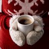 Woman in red Christmas sweater and mittens hold a hot seaming cup of coffee.