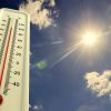 Thermometer measures high heat against summer sky.