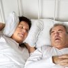 Senior couple in bed and wife covers ears due to snoring husband.