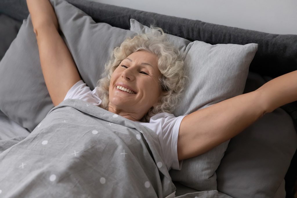 Senior woman smiling with arms extended after a good night's sleep.