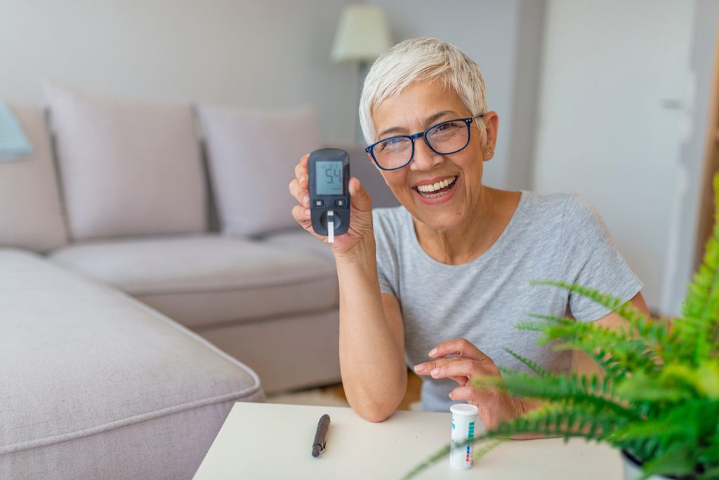 Senior woman diabetes patient smiling and holding up her glucometer.