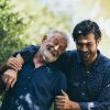 Elderly man and his son laughing and hugging while on an outdoor walk.