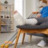 Senior man with broken leg sitting in easy chair and talking on cell phone.