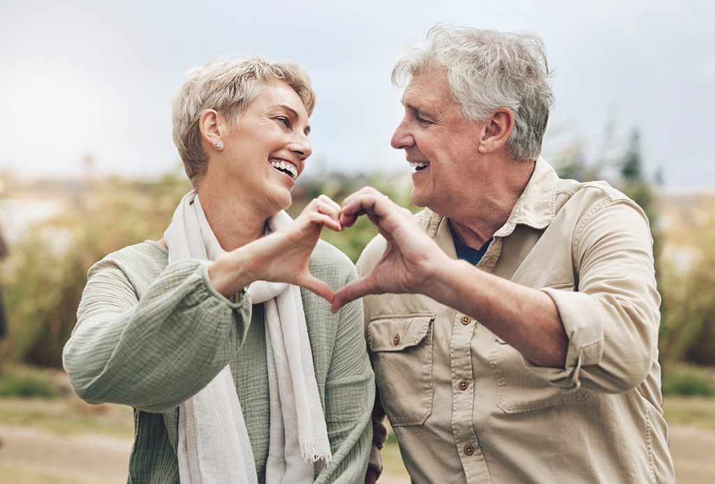 Senior couple smiling and forming a heart with their hands.